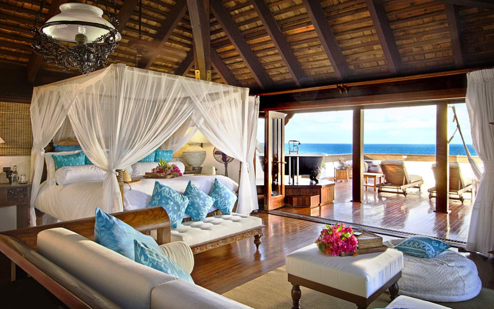 Ortasında beyaz gölgelik yatak bulunan okyanus kıyısındaki bungalovun harika açık alan tasarımı